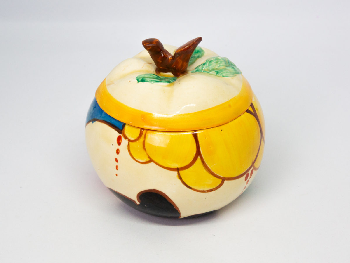 Apple shaped preserve pot by Clarice Cliff. A fun, funky hand-painted preserve pot in the Fantasque Bizarre line, 'Summerhouse' pattern. In excellent condition. Signed to the base. c1931-1933. Measures 50mm in diameter at base, 95mm at bulbous middle and approximately 85mm at tallest. Another angle of pot showing mostly the yellow bubble pattern with hint of blue pattern visible to the left.