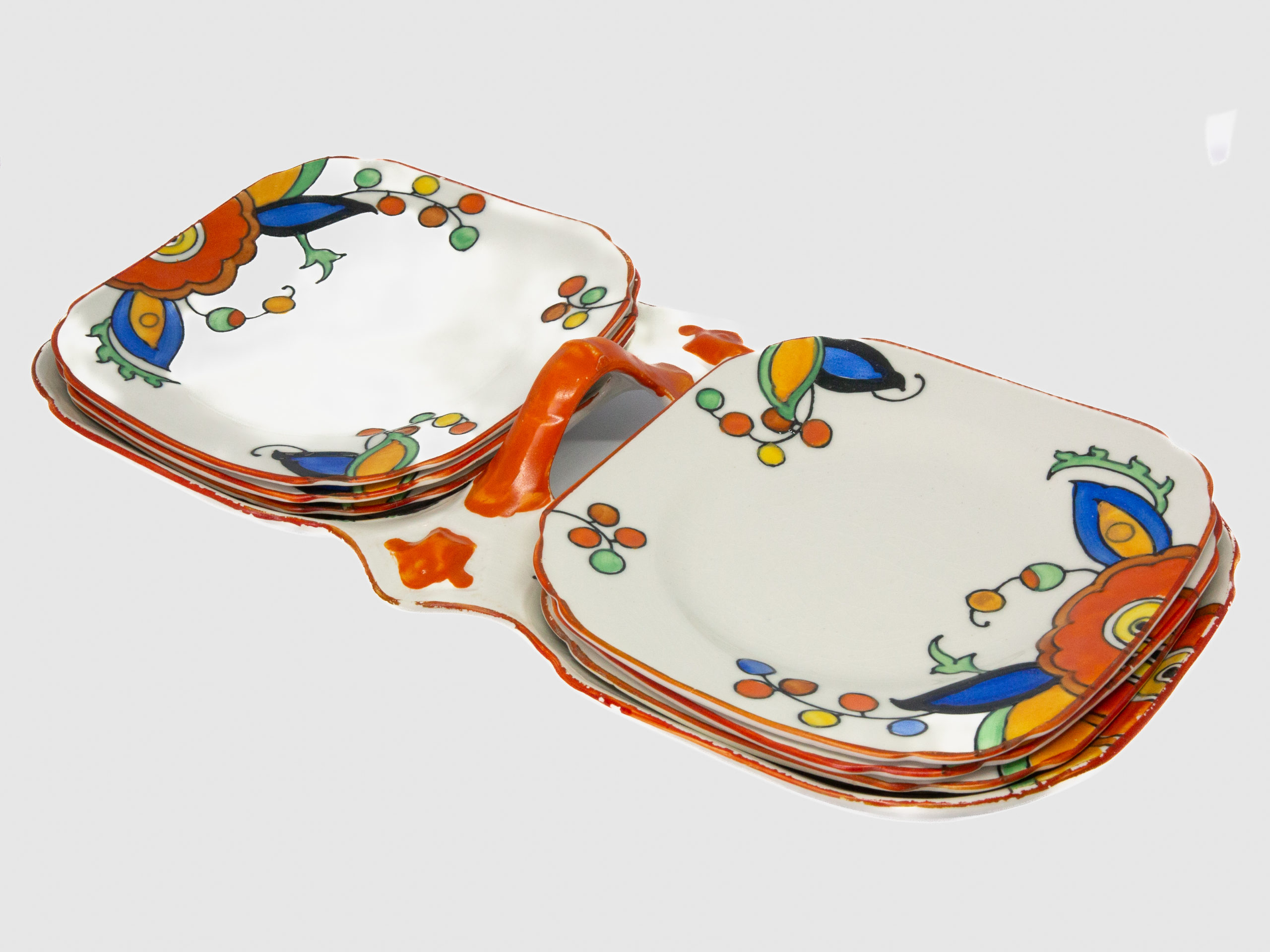 Art Deco sandwich set by Charlotte Rhead. A pretty and practical set comprising of a serving plate/tray with 2 shallow dish shaped plates connected with a handle to the centre and 6 small square side plates. Hand-painted in cheerful bright vibrant colours to cheer up any occasion. Design number 4133 'New Jazz' pattern c1928-1929. Each piece marked with the green Burleigh ware stamp with Rhead signature on the base of the serving plate. Visible crazing to each piece and some wear around the edge, especially around serving plate. Each small plate measure 145mm square and the serving plate/tray measures 330mm long,150mm wide and approximately 50mm tall by handle. Main photo showing the whole set as it comes with 3 side plates each on each side of the serving platter.