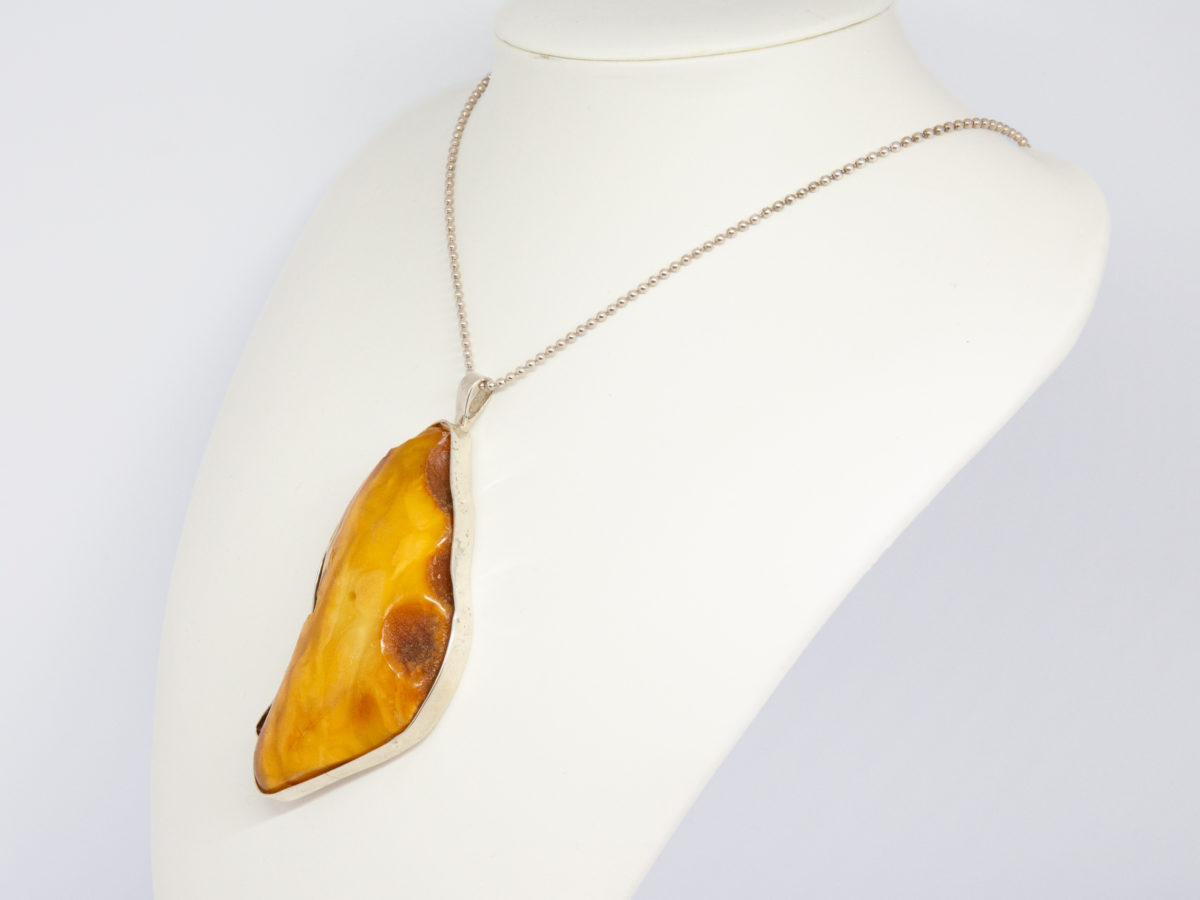 Rare large egg yolk amber pendant and chain. Stunning huge egg yolk amber set in a sterling silver frame on a sterling silver ball chain. Hallmarked to the pendant bail for London assay c1997 and 925 on the chain clasp. Pendant drop length 95mm and 45mm at widest. Photo of necklace displayed at an angle on a stand with pendant facing left