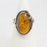 1960s vintage silver and amber ring. Pretty honey amber set on sterling silver with an Art Nouveau style decorative touch to one side. Worn hallmark to the outside band of ring at the back. Ring front measures 25mm by 20mm. Ring size O.5 / 7.5. Main photo of ring displayed on a cone shaped stand and seen face on.