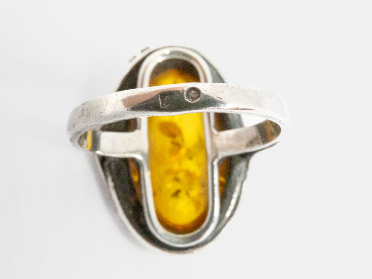 1960s vintage silver and amber ring. Pretty honey amber set on sterling silver with an Art Nouveau style decorative touch to one side. Worn hallmark to the outside band of ring at the back. Ring front measures 25mm by 20mm. Ring size O.5 / 7.5. Close up photo of the hallmark on the outside of ring band at the back.