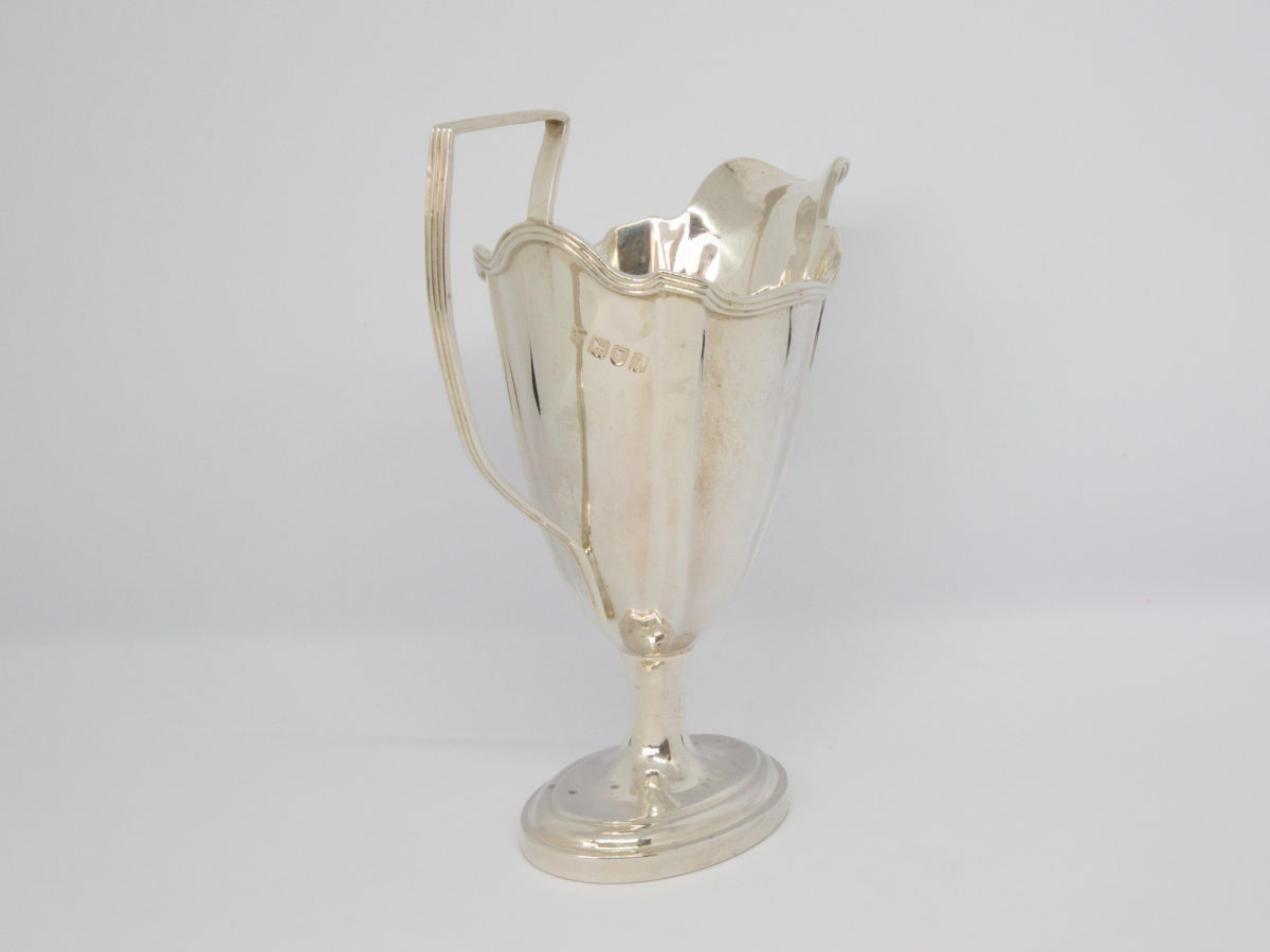 Antique sterling silver milk or cream jug. Aesthetically stunning jug by Thomas Bradbury of London c1904. Full hallmark to back of jug by handle. Base measures 63mm by 44mm, 110mm at widest from tip of spout to handle edge and 136mm at tallest at handle. Photo of jug at an angle with handle in the bottom left corner and spout facing top right.