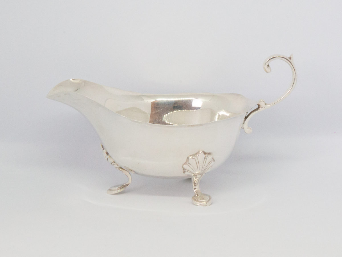 Vintage sterling silver cream or sauce jug. Simple but elegant jug with scallop detail to the legs and an open curl handle. Full hallmark to the base for Birmingham assay and made by Elkington & Co c1938. Main photo of jug seen from a near eye level angle with spout to the left and handle to the right of photo.