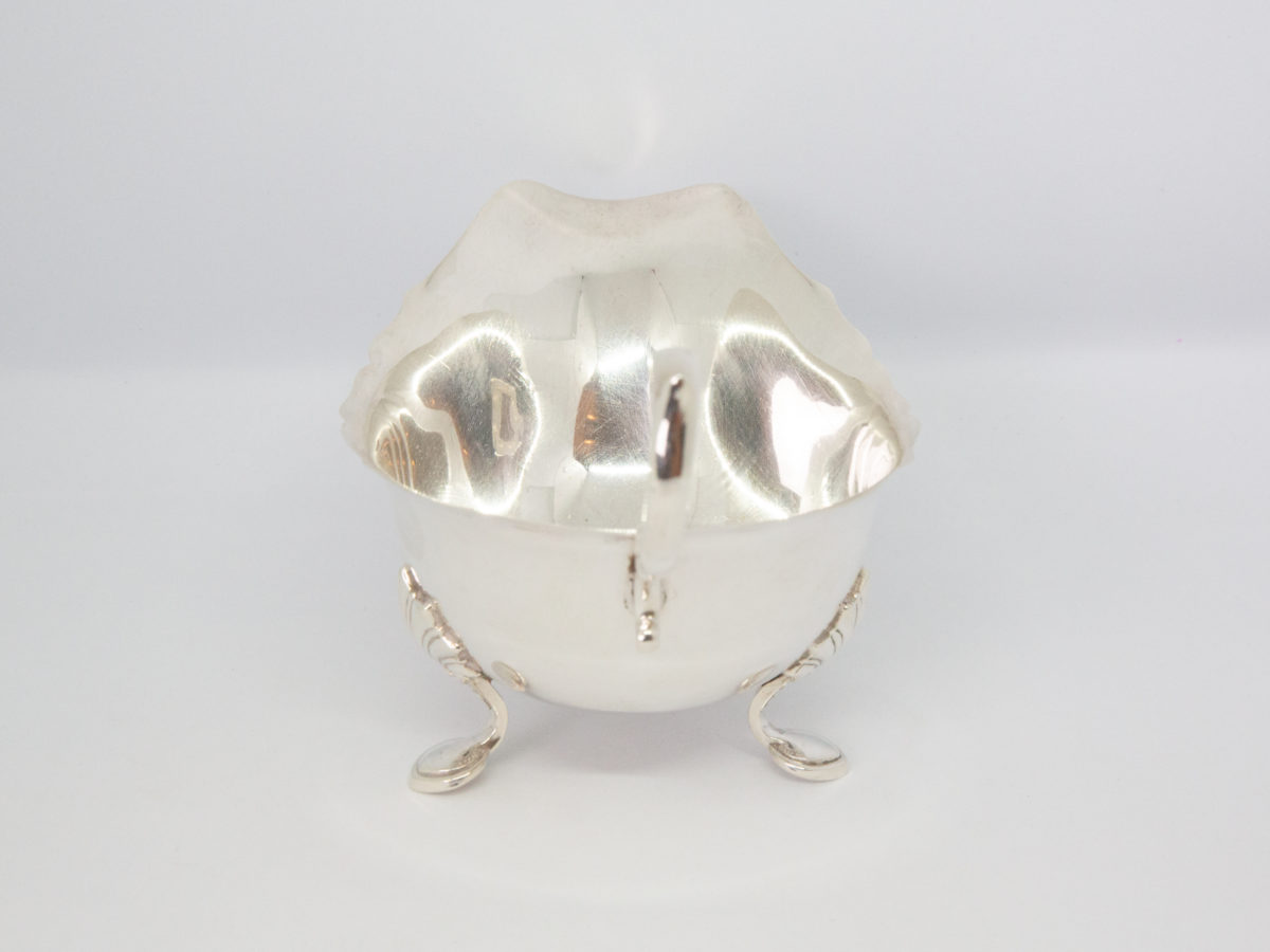 Vintage sterling silver cream or sauce jug. Simple but elegant jug with scallop detail to the legs and an open curl handle. Full hallmark to the base for Birmingham assay and made by Elkington & Co c1938. Photo of jug from the back handle side