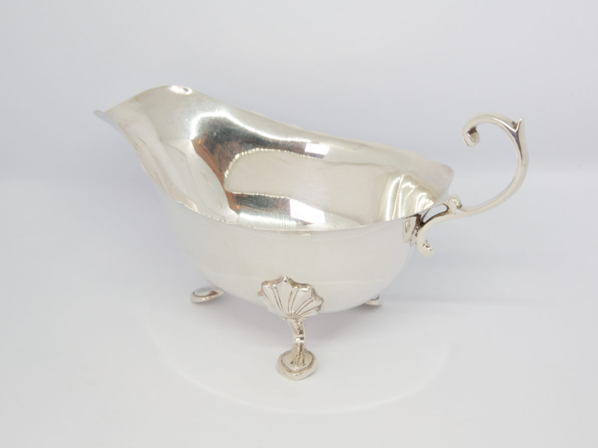 Vintage sterling silver cream or sauce jug. Simple but elegant jug with scallop detail to the legs and an open curl handle. Full hallmark to the base for Birmingham assay and made by Elkington & Co c1938. Photo of ring at a diagonal angle & raised with spout in the top left corner and inside of the jug shown.