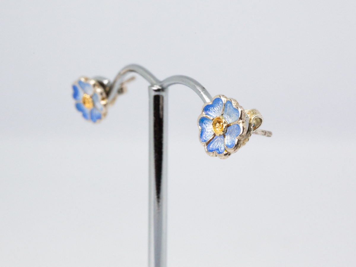 Vintage Sheila Fleet enamelled silver earrings. A sweet pair of sterling silver stud earrings in a flower shape with blue enamel to the petals by Sheila Fleet, Orkney Islands. Hallmarked 925 on stud post and butterfly. Original Sheila Fleet box included. Flowers measure approximately 8mm in diameter and weigh 1.7gms. Photo of earrings on a display stand and shown at an angle with earring fronts facing left of photo.