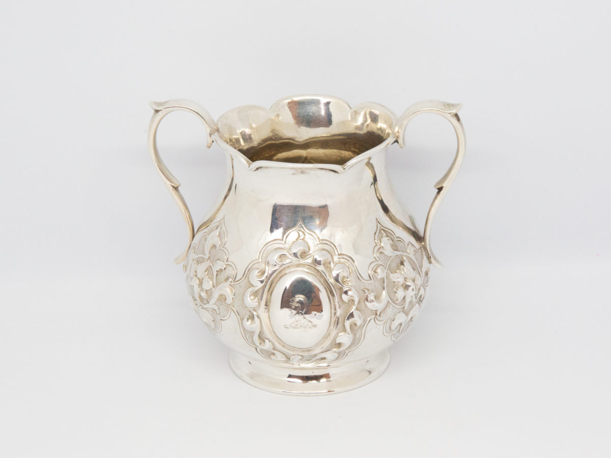 Antique 2 handled sterling silver pot. Small 2 handled sterling silver pot with intricate relief pattern around the lower bulbous area. One cartouche has a profile of a medieval knight engraved to it while other cartouche is empty - for a damsel perhaps? Shapely handles and rim add to the elegance of this piece. Full hallmark to the base for London assay c1875. Made by Francis Higgins. Base measures 55mm in diameter, width across handles measures approximately 105mm and opening at top 60mm in diameter. Photo of pot seen from the side with engraved knight cartouche.