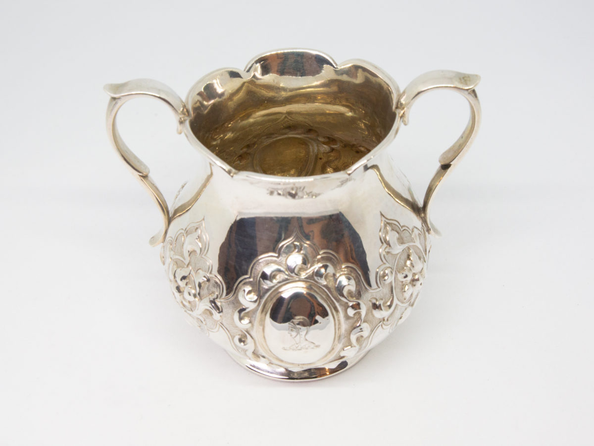 Antique 2 handled sterling silver pot. Small 2 handled sterling silver pot with intricate relief pattern around the lower bulbous area. One cartouche has a profile of a medieval knight engraved to it while other cartouche is empty - for a damsel perhaps? Shapely handles and rim add to the elegance of this piece. Full hallmark to the base for London assay c1875. Made by Francis Higgins. Base measures 55mm in diameter, width across handles measures approximately 105mm and opening at top 60mm in diameter. Photo of pot from the engraved knight side and seen from a slightly raised angle peering into the cup.
