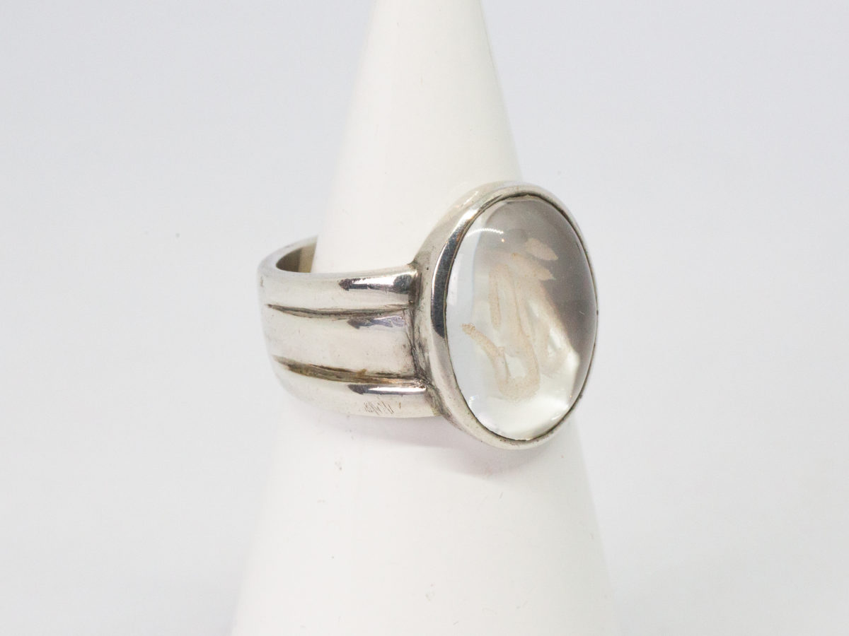 Modern vintage ring in sterling silver with Om crystal. An unusual modern vintage sterling silver ring set to the centre with smooth oval quartz crystal with the Om symbol carved into it. Crystal area measures 18mm by 10mm. Ring size P / 7.5. Photo of ring on a cone shaped stand with ring front facing right of picture.