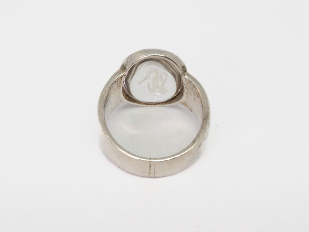 Modern vintage ring in sterling silver with Om crystal. An unusual modern vintage sterling silver ring set to the centre with smooth oval quartz crystal with the Om symbol carved into it. Crystal area measures 18mm by 10mm. Ring size P / 7.5. Photo of ring on a flat surface with ring front facing away from shot.