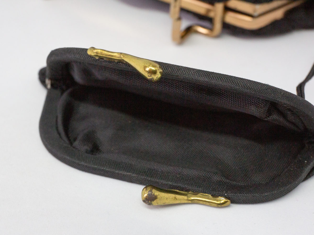 40s Black fabric bag with brass clasp. A lovely 40s bag in black fabric with a floral accent. Interior has a small pocket and a tiny coin purse attached to string. Brass clasp and short black fabric handle completes the look. Drop length from handle to bottom of bag is 300mm. Close up the coin purse with clasp undone.