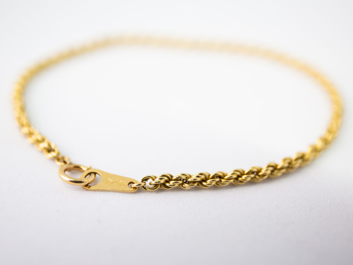 Vintage 18 karat gold rope chain bracelet. Fine rope chain bracelet in 18 karat yellow gold. Hallmarked 750 for 18 karat gold. Photo of bracelet on a flat surface and seen from the clasp area.