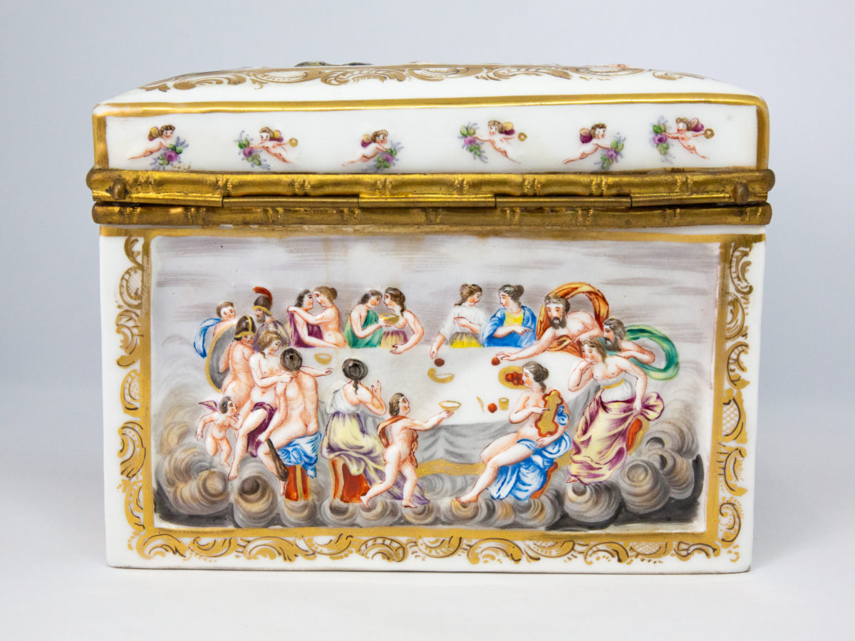 Late 19th century Naples porcelain box. A heavy porcelain box moulded in high relief with scenes of scantily clad men and women disporting themselves in various ways. Beautifully hand-painted in bright vibrant colours and finished off with gilt accent. Photo of the decoration on the back of the box showing a scene of wining and dining around a large oval table.
