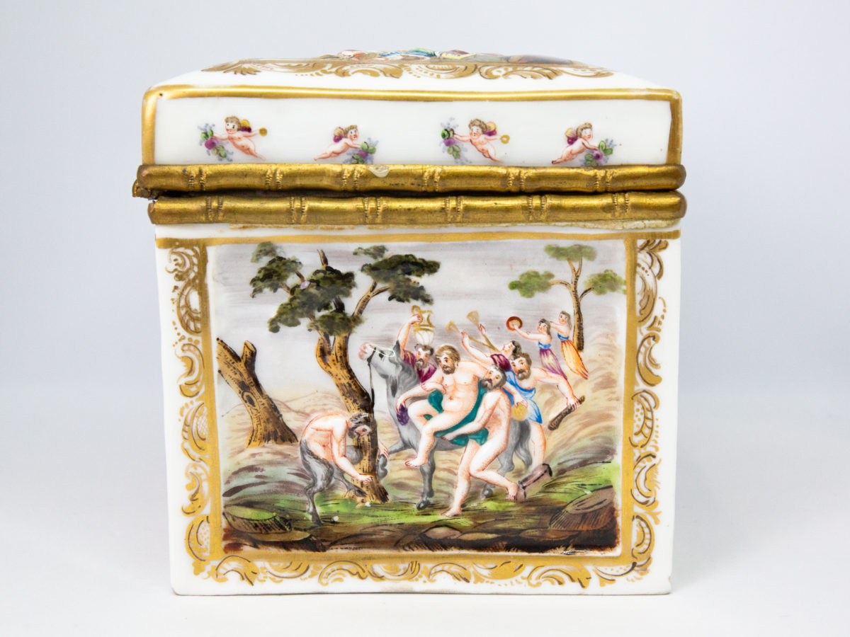 Late 19th century Naples porcelain box. A heavy porcelain box moulded in high relief with scenes of scantily clad men and women disporting themselves in various ways. Beautifully hand-painted in bright vibrant colours and finished off with gilt accent. Photo of other side of box showing scene of a man being helped off his horse and presented in front of the God Pan
