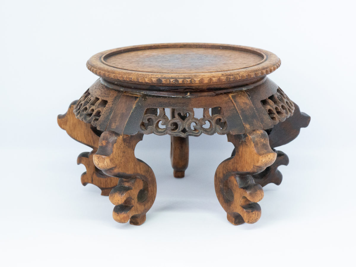 Vintage carved Chinese wooden stand. A nice sized Chinese stand in natural wood with lovely carved detail to the skirt under the stand and to the legs. Some repair work has been carried out as shown on photos. Outer diameter of top area measures 126mm and inner diameter measures 103mm. Widest area at top of legs measures 165mm. Photo of stand from another side showing the different colouration of the wood.