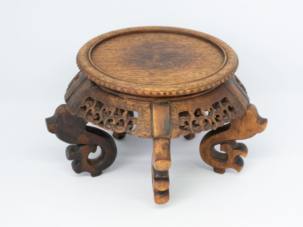Vintage carved Chinese wooden stand. A nice sized Chinese stand in natural wood with lovely carved detail to the skirt under the stand and to the legs. Some repair work has been carried out as shown on photos. Outer diameter of top area measures 126mm and inner diameter measures 103mm. Widest area at top of legs measures 165mm. Photo of stand seen from a slight raised angle showing the flat top.