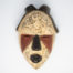 Small vintage wooden African mask. Lovely African mask carved from one piece of wood and coloured in natural pigment. Has a sweet smiling facial expression-even looks as though it is blowing kisses from certain angles- and an unmistakeable aroma of bonfires. Main photo of mask laid on a flat surface and looking straight down from above.