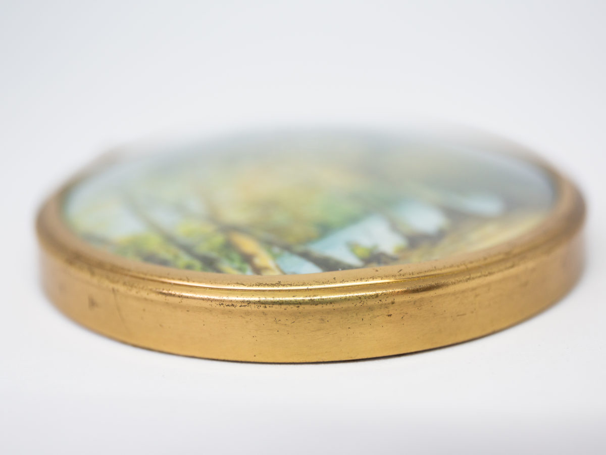 Hand-painted miniature with brass frame. Lovely hand-painted miniature of a man fishing by the river under the trees and a second person asleep. Wonderful detail to this piece of art. Measures 75mm in diameter. Drop length from top of bail measures 92mm. Close up photo of the outer rim of the frame.