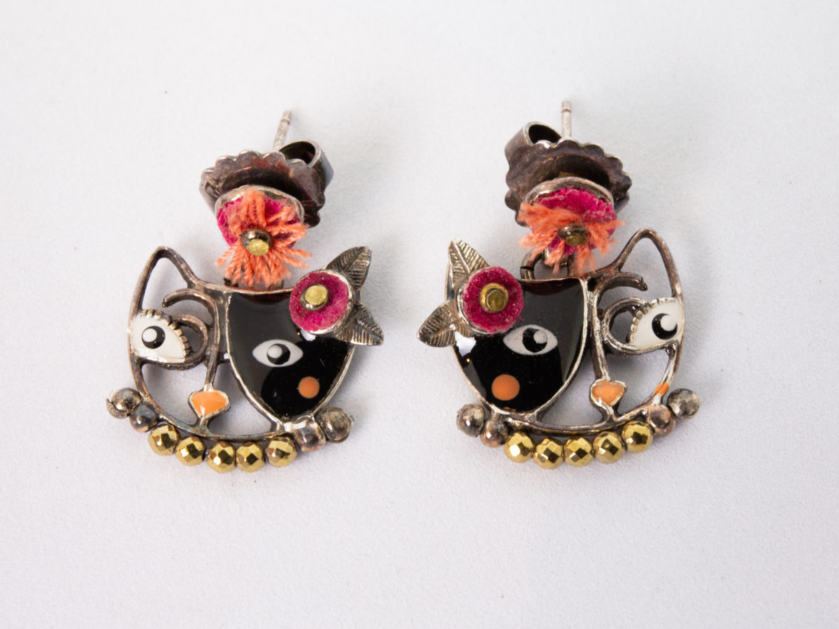 Modern pair of pretty cat earrings. Pretty pair of pampered cat earrings by the wonderful Taratata. Metal with enamel and pink felt flowers. Has a Picasso-esque look. Super large butterfly for secure fastening. Signed Taratata to the back. Drop length approximately 22mm and 18mm at widest. Main photo of both earrings laid side by side on a flat surface and shown looking away from each other.