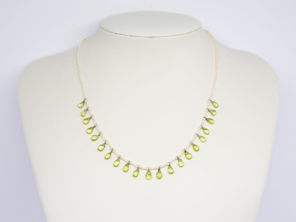 Modern seed pearl and peridot necklace. Very pretty and dainty necklace of seed pearls with teardrop faceted peridot briolette beads to the front finished with a gilt silver clasp. Very elegant classical look. (Some gilt wear to ring clasps). Main photo of necklace displayed on a white display stand and seen forward facing.