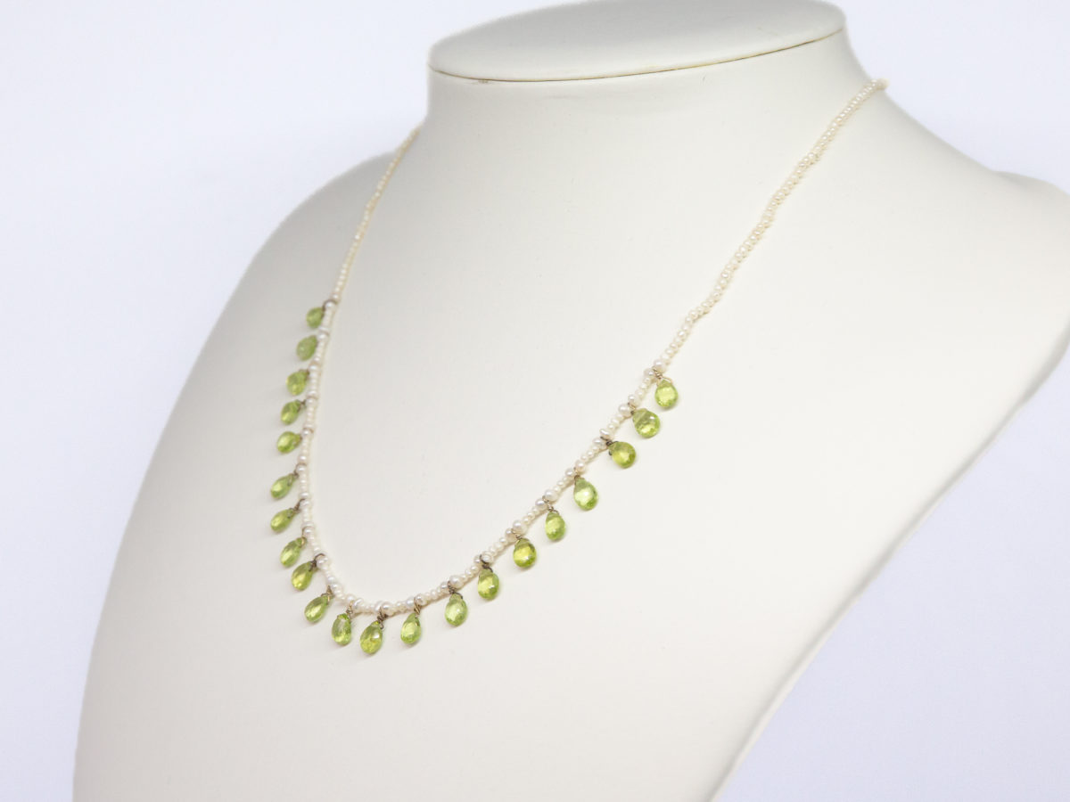 Modern seed pearl and peridot necklace. Very pretty and dainty necklace of seed pearls with teardrop faceted peridot briolette beads to the front finished with a gilt silver clasp. Very elegant classical look. (Some gilt wear to ring clasps). Photo of necklace on a white display stand and seen from an off side angle
