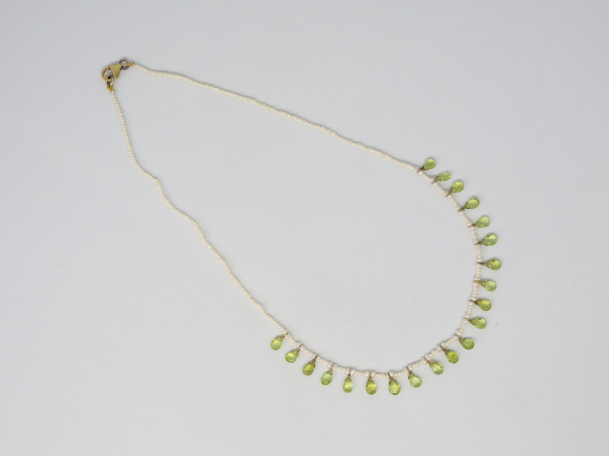Modern seed pearl and peridot necklace. Very pretty and dainty necklace of seed pearls with teardrop faceted peridot briolette beads to the front finished with a gilt silver clasp. Very elegant classical look. (Some gilt wear to ring clasps). Photo of necklace displayed on a flat surface with clasp end to the top left of photo.