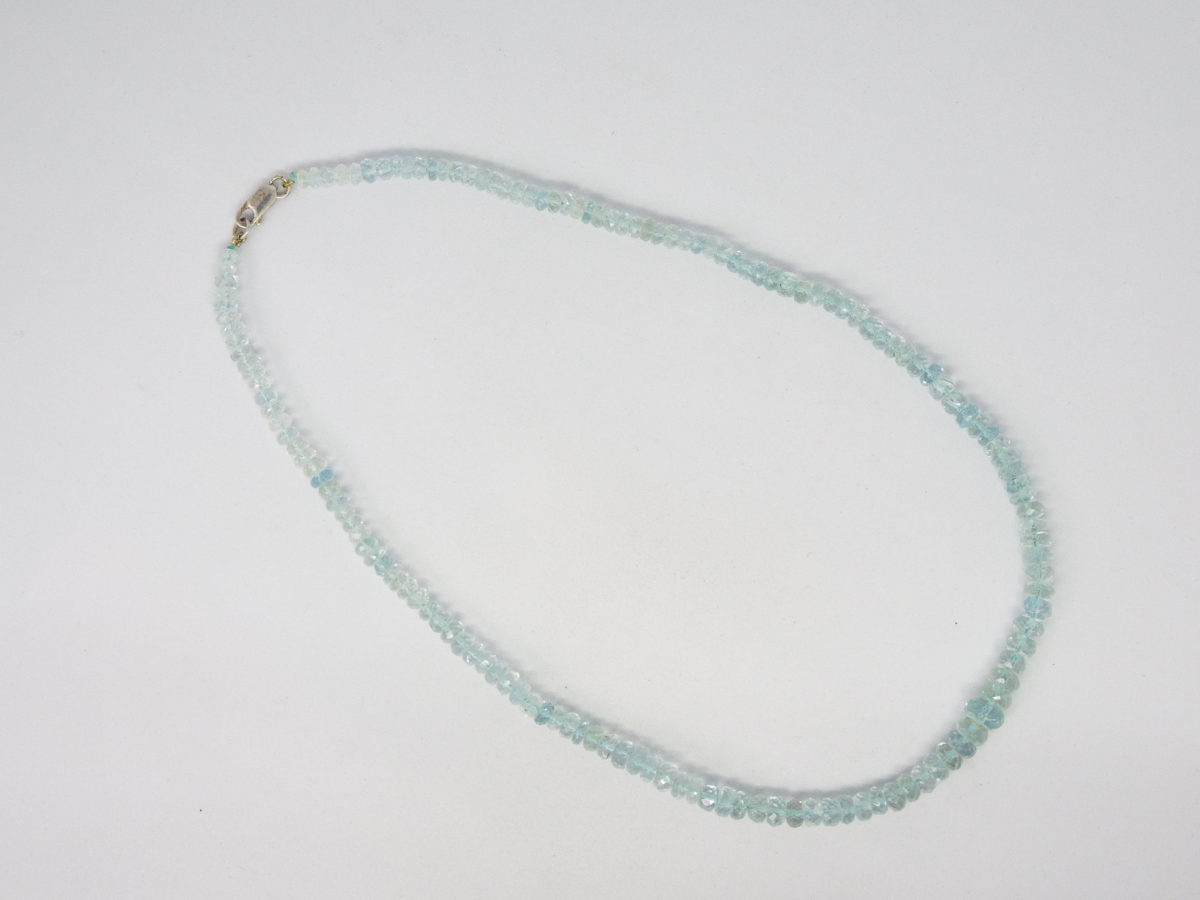 Modern aquamarine bead necklace. Pretty necklace made up entirely of graduating faceted aquamarine stones beautifully strung and finished with a sterling silver clasp. Photo of necklace laid out on a flat surface and displayed in a ring with clasp fastened.