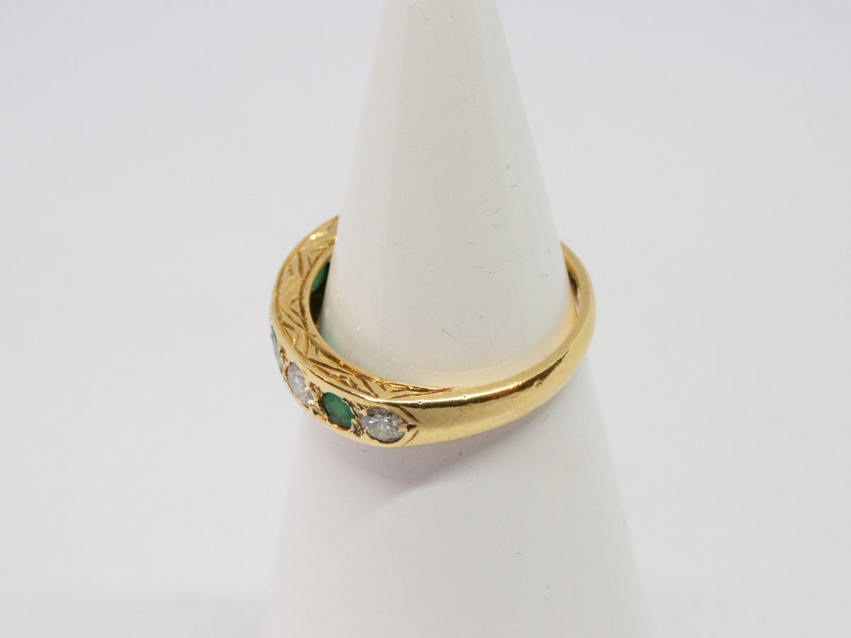 Vintage 18 karat gold ring with emeralds and diamonds. A stunning 18 karat gold ring set with 4 emeralds and 5 diamonds in an alternating row. Fully hallmarked for Sheffield assay c1975. Box included. Ring size O.5 / 7.25. Ring weight 3.8gms. Photo of ring on a cone shaped display stand and seen from a side angle.