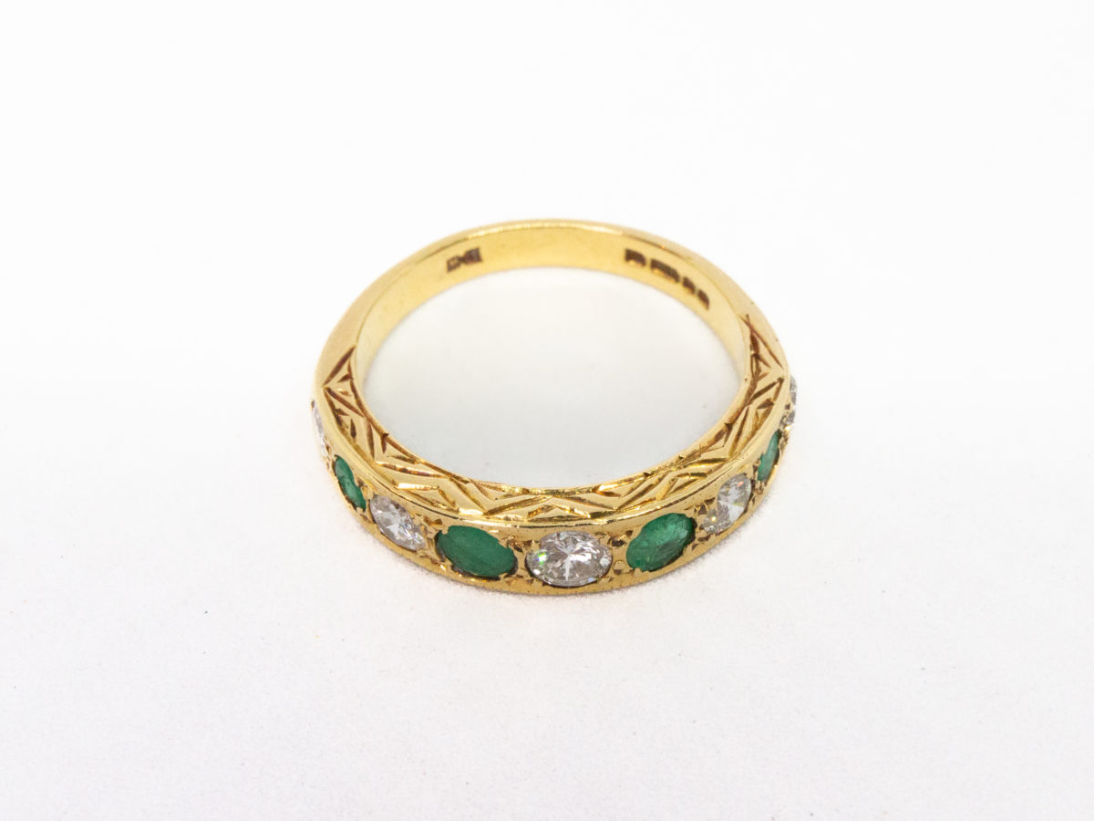 Vintage 18 karat gold ring with emeralds and diamonds. A stunning 18 karat gold ring set with 4 emeralds and 5 diamonds in an alternating row. Fully hallmarked for Sheffield assay c1975. Box included. Ring size O.5 / 7.25. Ring weight 3.8gms. Photo of ring on a flat surface and seen from a raised angle with ornate gallery visible.