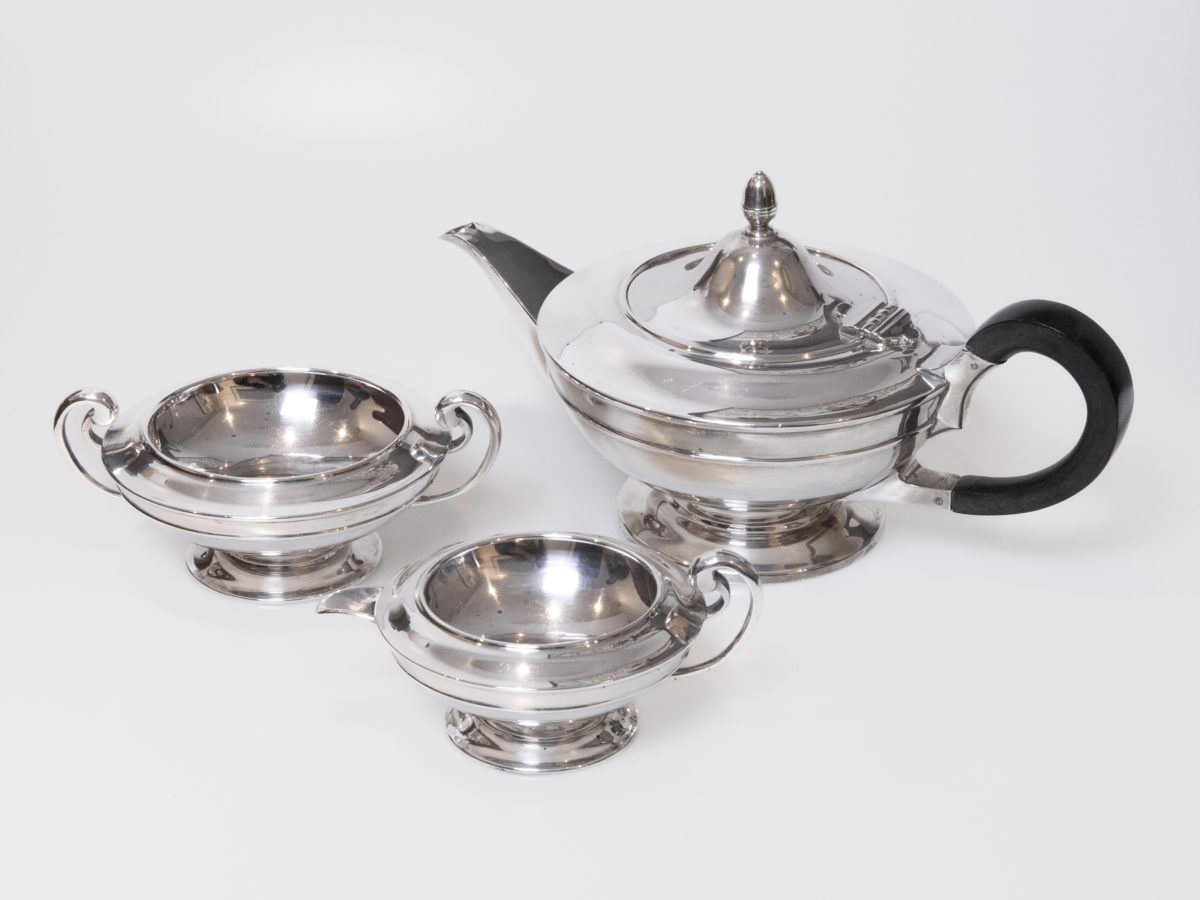 Antique Art Deco sterling silver tea set trio. A handsome sterling silver trio consisting of tea pot, sugar bowl and milk jug all in a very aesthetic Art Deco shape. Each piece is stamped to the base for Goldsmiths and Silversmiths Company 112 Regent Street and also fully hallmarked for Sheffield assay. The tea pot is dated for 1918, weighs 723.4gms and measures 102mm in diameter at base, 160mm in diameter at widest at top of body, 175mm wide from tip of spout to handle and 145mm tall at finial. There is also a etched picture of a thistle with motto 'Dulcius ex Asperis' (Sweeter after difficulties). The sugar bowl is dated for 1917, weighs 266gms and measures 70mm in diameter at base, 125mm in diameter at widest at top, 160mm at widest across handles, 60mm tall at main body and 65mm tall at handles. The jug is also dated for 1917, weighs 183gms and measures 64mm in diameter at base, 105mm in diameter at top, 145mm at widest from tip of spout to handle, 52mm tall at body and 65mm at tallest by handle. Main photo of all three pieces displayed together on a plain flat surface with teapot to the top right, sugar bowl to mid left and jug to centre front.