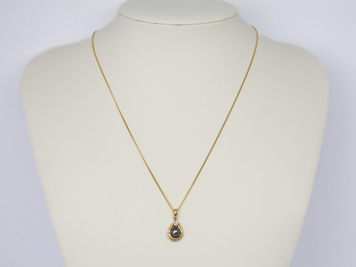 9 karat gold pendant set with a black pearl & small diamond on a 9 karat gold chain. Very pretty modern 9 karat gold necklace and small pendant with a black pearl to the centre and small round cut diamond above. Elegant and eye catching. Full hallmark to pendant bail and chain clasp. Small box included. Pendant drop length 18mm. Necklace weight 2.6gm. Main photo showing necklace displayed on a white display stand and seen from the front.
