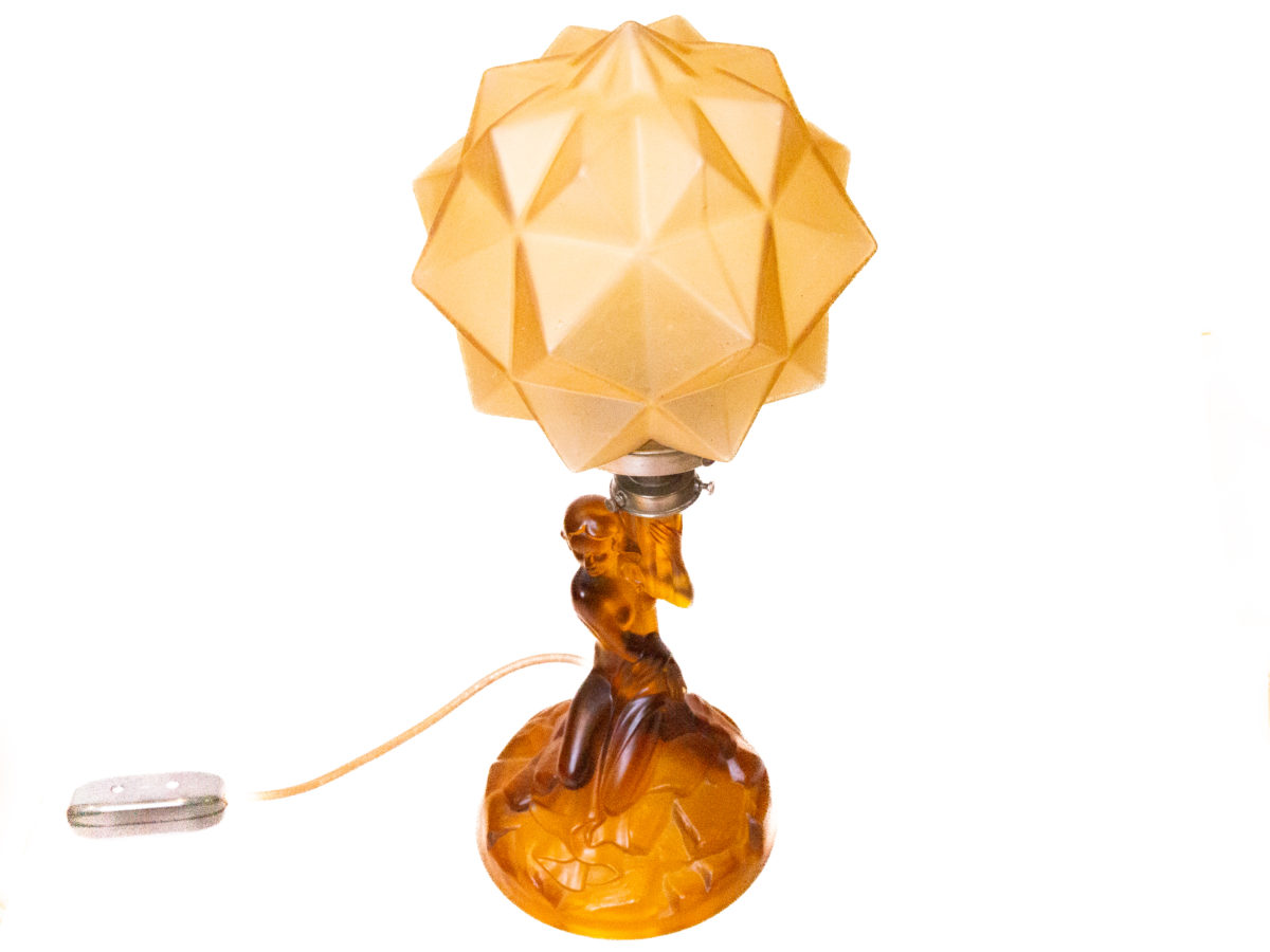 Art Deco glass lamp and shade. Stunning amber glass lamp of semi naked seated lady holding a multi dimensional amber glass shade. The shade is a slightly lighter colour to the main lamp. Lamp base measures 145mm in diameter. Photo of lamp from a slightly raised angle looking just a little bit downward.