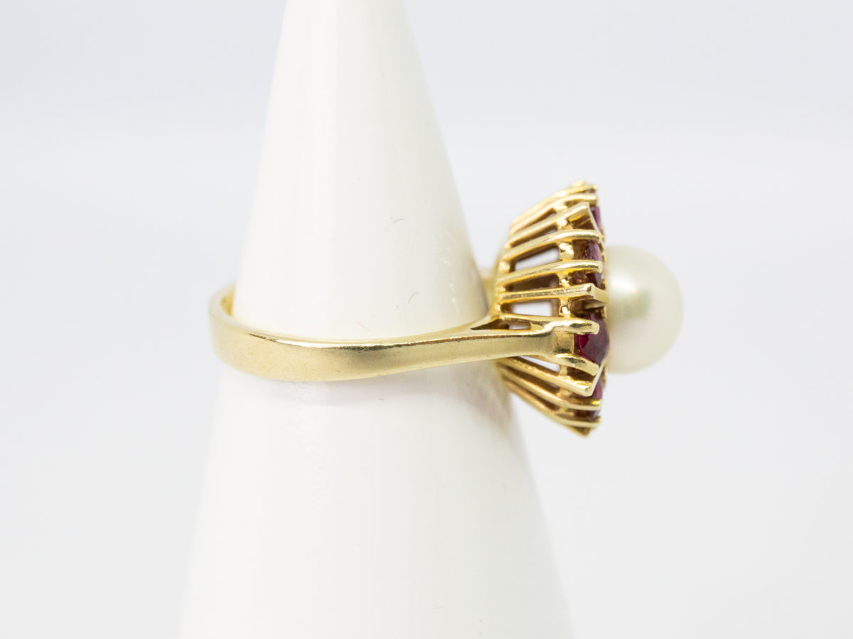 Vintage 14 karat gold ring with pearl and rubies. Pretty ring with a central pearl framed by 8 round cut rubies in a star/sun burst design on an open prong cathedral setting. Ring size N.5 / 7. Ring weight 5.6gms. Photo of ring on a cone shaped stand with ring front facing right.