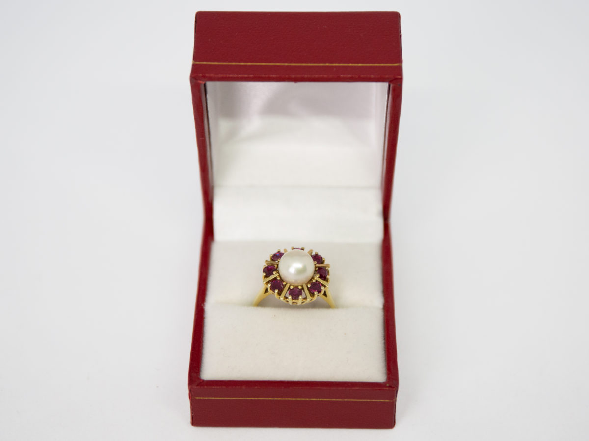 Vintage 14 karat gold ring with pearl and rubies. Pretty ring with a central pearl framed by 8 round cut rubies in a star/sun burst design on an open prong cathedral setting. Ring size N.5 / 7. Ring weight 5.6gms. Photo of ring displayed in a red and white ring box giving a more festive look than it already has!