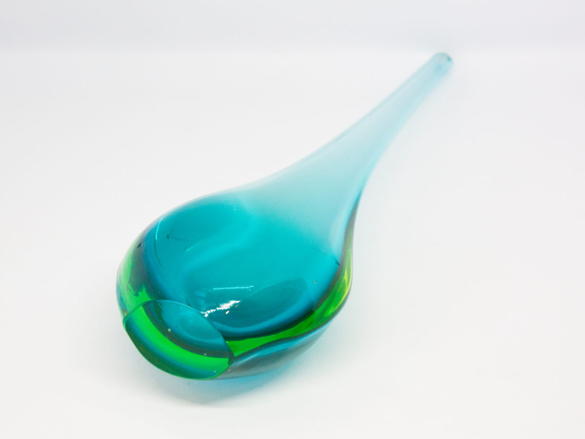 Vintage turquoise glass vase by Murano. Striking slender sommerso glass vase by Murano in stunning turquoise with vibrant sea green to the lower sides. The aesthetically stunning shape is akin to a drop of water and is very pleasing to the eye. A wonderful vintage glass art attributed to Flavio Poli. c1960s. Base measures 42mm by 30mm, the bulbous lower are measures 90mm wide by 60mm deep and top measures 12mm in diameter. The opening at top is very small measuring approximately 6mm in diameter. Photo of vase laid down on a flat surface and shown with base end to the bottom left foreground.