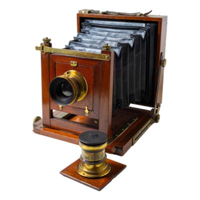 A Sands & Hunter Mahogany & Brass Half Plate Camera circa 1895 with two lenses and two plate holders. COLLECT FROM STORE ONLY. Main photo showing camera set at a diagonal angle with camera front facing bottom left and one of the lenses posed at the foot of camera front.