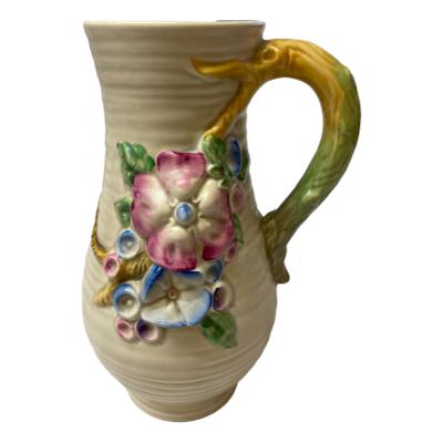 The Clarice Cliff vase is highly decorative featuring a series of colourful flowers in relief cascading down the body and a handle on one side. COLLECT FROM STORE ONLY. Main photo of vase from the side with most floral decoration. Handle is to the right.