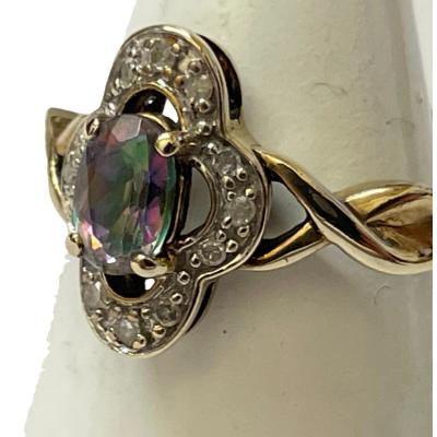 A 9ct gold Gypsy ring size M with a colourful Mystic stone and diamond setting. Close up photo of the ring front shown from a side angle with ring front facing towards the left.