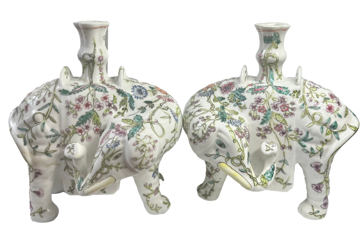 A pair of vintage Chinese export hand-painted elephant candle holders. One elephant candle holder is in perfect condition. The other has had an old repair to the base of the candle holder & back leg. Please see last two photos. COLLECT FROM STORE ONLY. Close up photo of the 2 elephants side by side facing each other but heads turned away from each other.