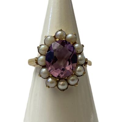 Antique style 9 karat gold ring set with a generously sized oval cut pale purple amethyst to the centre within a seed pearl frame. Full hallmark for Birmingham assay c1992. Ring size P / 7.5. Main photo of ring displayed on a cone shaped stand and seen with ring front forward facing.
