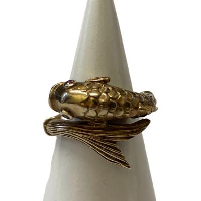 Vintage 9 karat gold ring in the form of a fish swimming in a turn with head and tail forming the ring front. Lovely detailing of fins and scales makes this ring extra special. 2 small rubies make up the eyes to complete this wonderful goldfish! Full hallmark to inside band for London assay c1958. Ring size J / 5. Main photo of ring displayed on a cone shaped stand with fish head faced to the left and tail end to the right.