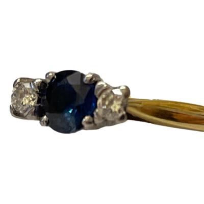 Vintage 18 karat gold trilogy ring set with a round cut sapphire of approximately 0.25 carat to centre with a 5 point sparkly diamond to either side. Ring size N / 6.75. Photo of ring from a side angle with ring front facing left.