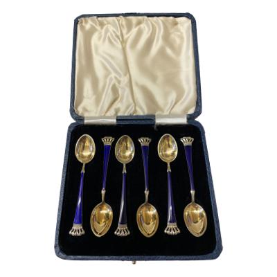 Cased set of 6 sterling silver and enamel spoons. Stunning set of 6 gilt silver spoons with cobalt blue enamel and a crown to handle tips. Made by Egon Laurissen (Ela) of Denmark. Full hallmark to back of each spoon which measure 95mm long. Main photo of spoons displayed inside their case and seen from a raised angle looking down from above.