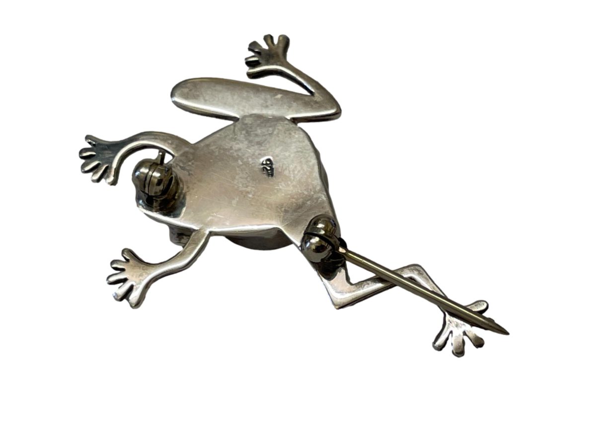 Vintage sterling silver brooch in the form of a frog in mid movement. The frog has light blue crystal glass eyes and its back is set with a round lapis lazuli cabochon. Hallmarked 925 for sterling silver. Close up photo of the back of brooch showing hallmark clearer. Pin is open.