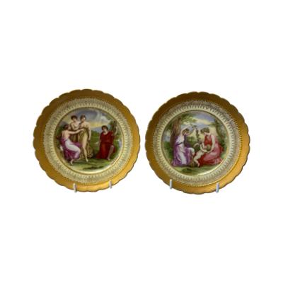 Pair of highly decorative side plates in neo classical Royal Vienna style. Both plates have heavy gilt edging and images of figures in brightly coloured neo classical dress. Each plate is signed Angelica Kauffman to the bottom of the images and marked with a beehive stamp and initials B&L to the back. Each measures approximately 155mm in diameter. Some signs of paint wear to both images. Main photo of both plates displayed upright and side by side.