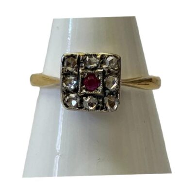 18 karat gold and platinum ring. Art Deco ring in 18 karat gold set with 8 small old mine rose cut diamonds and a 3 point ruby on a square platinum mount. Ring face measures 8mm square and weighs 2.1gms. Ring size N / 6.75. Main photo of ring on a cone shaped display stand with ring front facing forward.