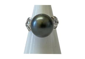 Tahitian black pearl and diamond ring. Huge natural black pearl set on 18 karat white gold with 14 baguette cut diamonds to each shoulder.  The pearl measures approximately 15mm round. Ring size N.5 / 7. Box included. Main photo of ring displayed on a cone shaped stand and seen from the front straight on.